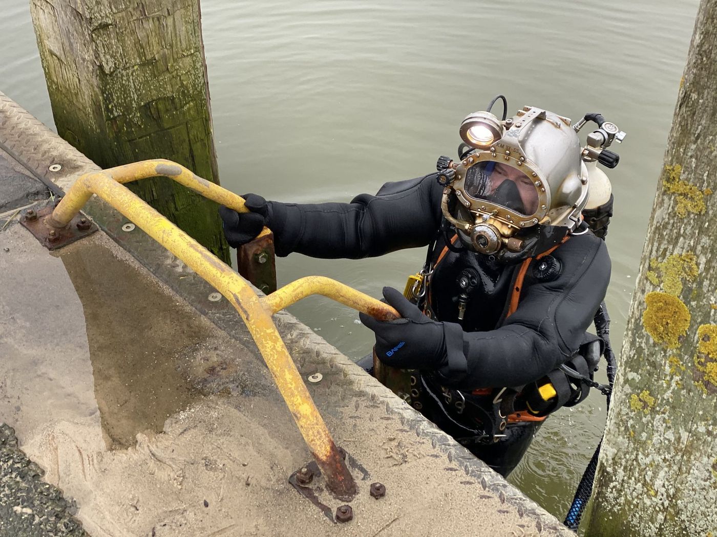 Helmtaucher mit Taucherhelm und Versorgungsschlauch steigt über eine Leiter aus dem Wasser